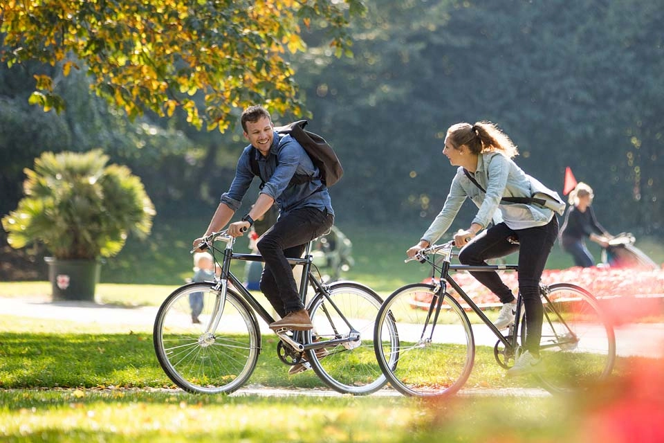 Zwei Radfahrer:innen fahren im Herbst durch den Park, Seitenansicht